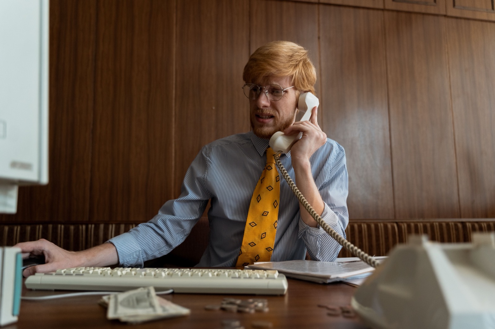 A man in a 90s office, on the phone, looking worried