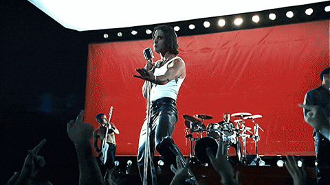 Singer of the band Creed in a white tank top and black leather pants on a stage with a red backdrop, one arm stretched out over a cheering crowd